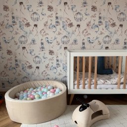 HouseOfDesign - Pokój dziecięcy z motywem morskim: łóżeczko, basen z kulkami i zabawka na tle tapety w balony, latarnie morskie i wieloryby. Jasne kolory, przytulna atmosfera.