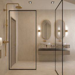 HouseOfDesign - Nowoczesna łazienka z kabiną walk-in, złotą deszczownicą i podwójną umywalką. Dwa owalne lustra z pionowymi lampami ściennymi nad marmurowym blatem. Jasne płytki i beżowe drzwi.