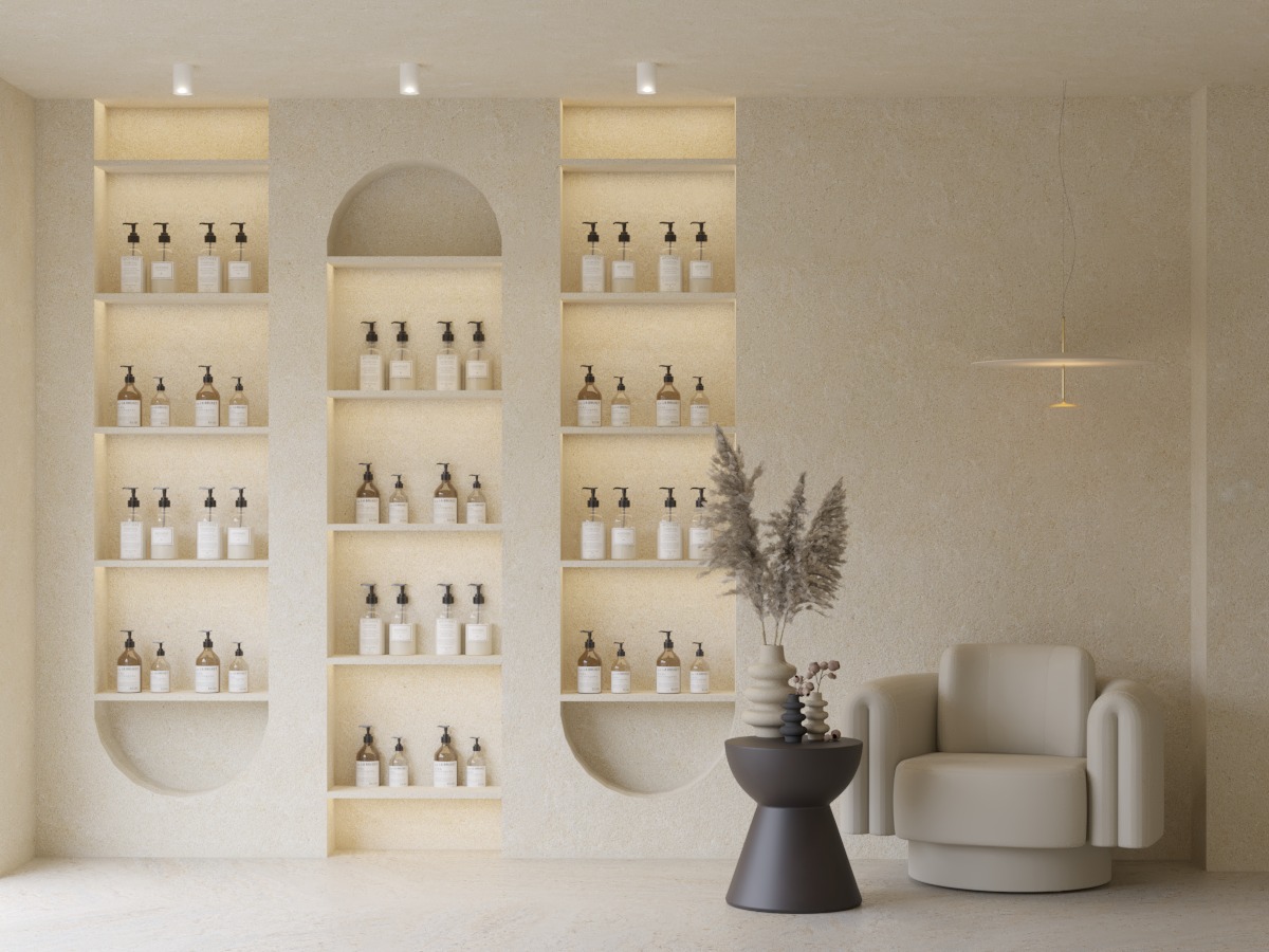 Minimalistyczne wnętrze: kremowe ściany z wnękami oświetlonymi punktowo, eksponujące kosmetyki. Obok fotel i stolik z dekoracjami, całość w ciepłej tonacji.