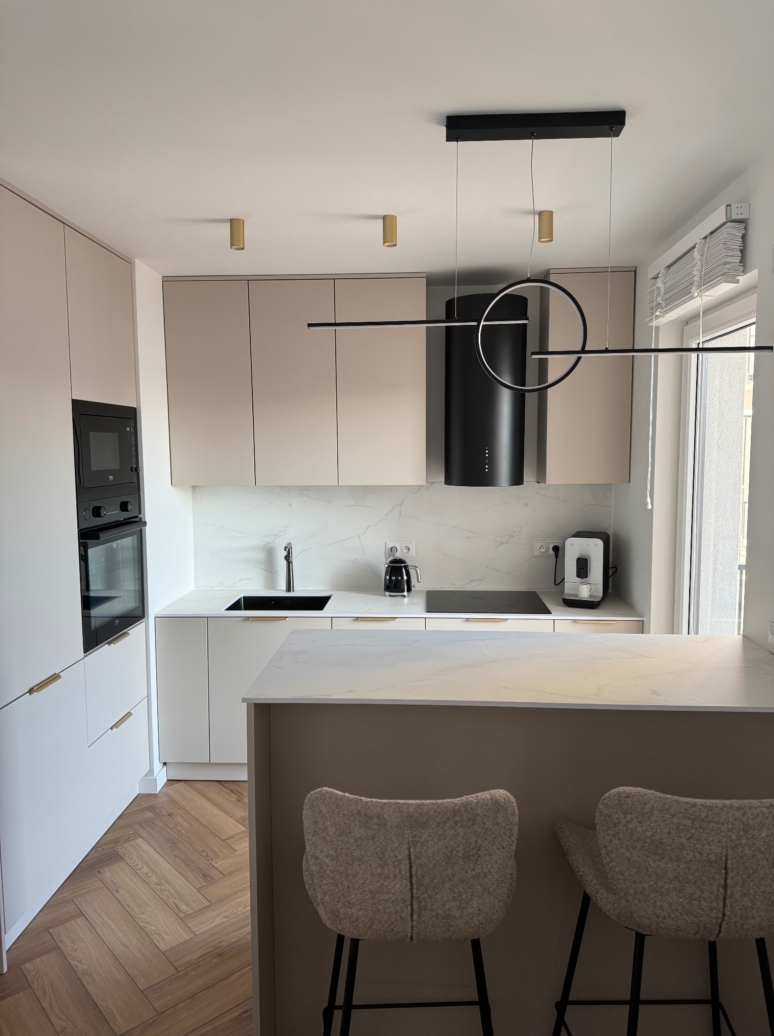 Elegancka kuchnia w beżach i bieli. Nowoczesne oświetlenie, marmurowe blaty, drewniana podłoga w jodełkę. Minimalistyczny design z wyspą i hokerami.