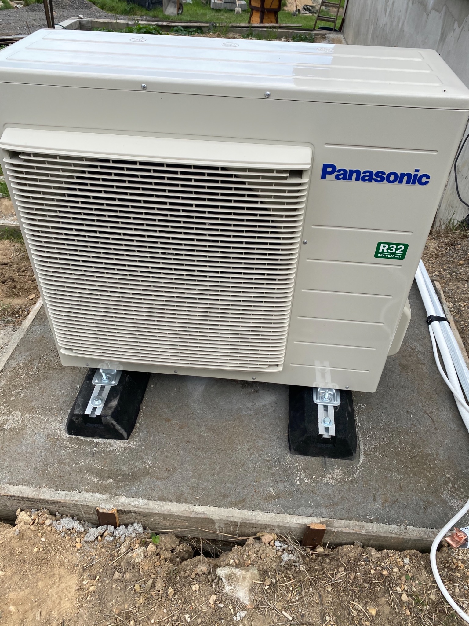 Zewnętrzna jednostka klimatyzacji Panasonic R32 zamontowana na betonowej podstawie z gumowymi podkładkami antywibracyjnymi, widoczne przewody.