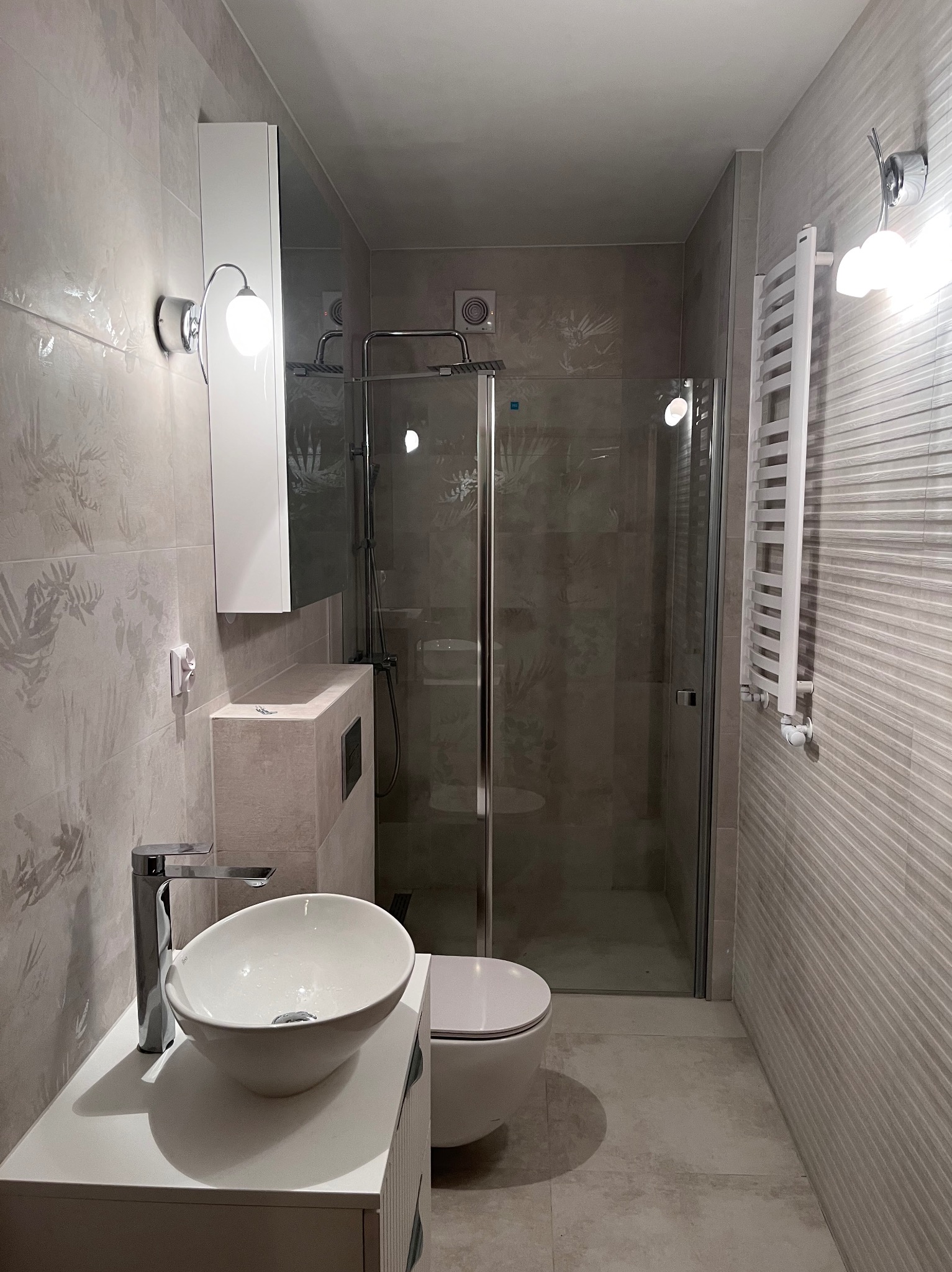 Nowoczesna łazienka w odcieniach szarości z kabiną prysznicową typu walk-in, umywalką nablatową i grzejnikiem drabinkowym. Minimalistyczny design, subtelne oświetlenie.