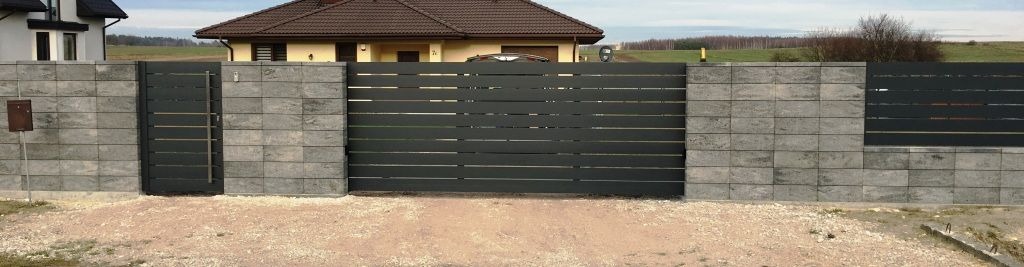 Nowoczesna, pozioma, grafitowa brama wjazdowa i furtka z szarymi, betonowymi słupkami i fragmentami ogrodzenia z tego samego materiału, widok z zewnątrz posesji.