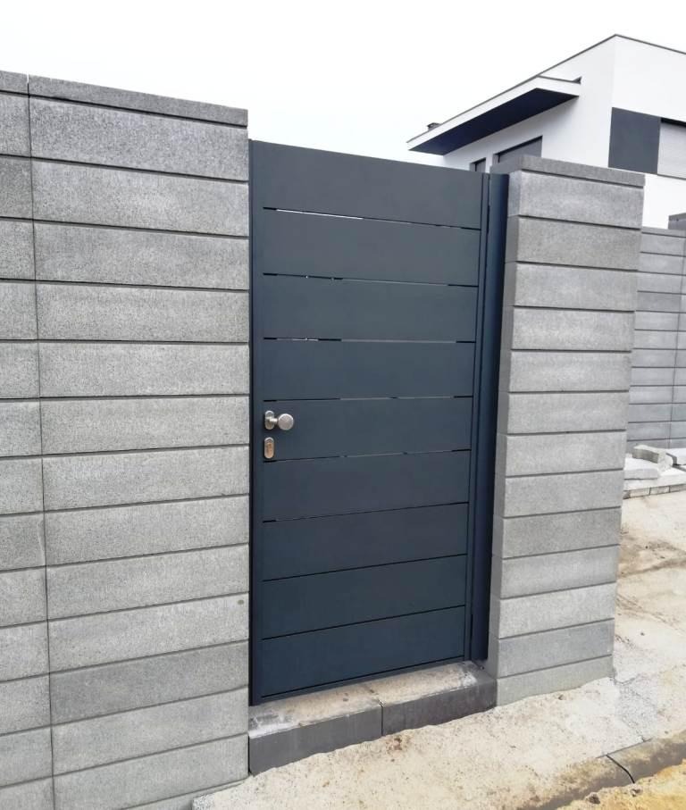Nowoczesna, antracytowa brama z poziomymi panelami, osadzona w słupkach z szarej kostki betonowej, na tle minimalistycznego domu.