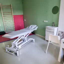 Jasne wnętrze gabinetu z profesjonalnym, białym, regulowanym łóżkiem do zabiegów, drabinką gimnastyczną, umywalką i krzesłem.