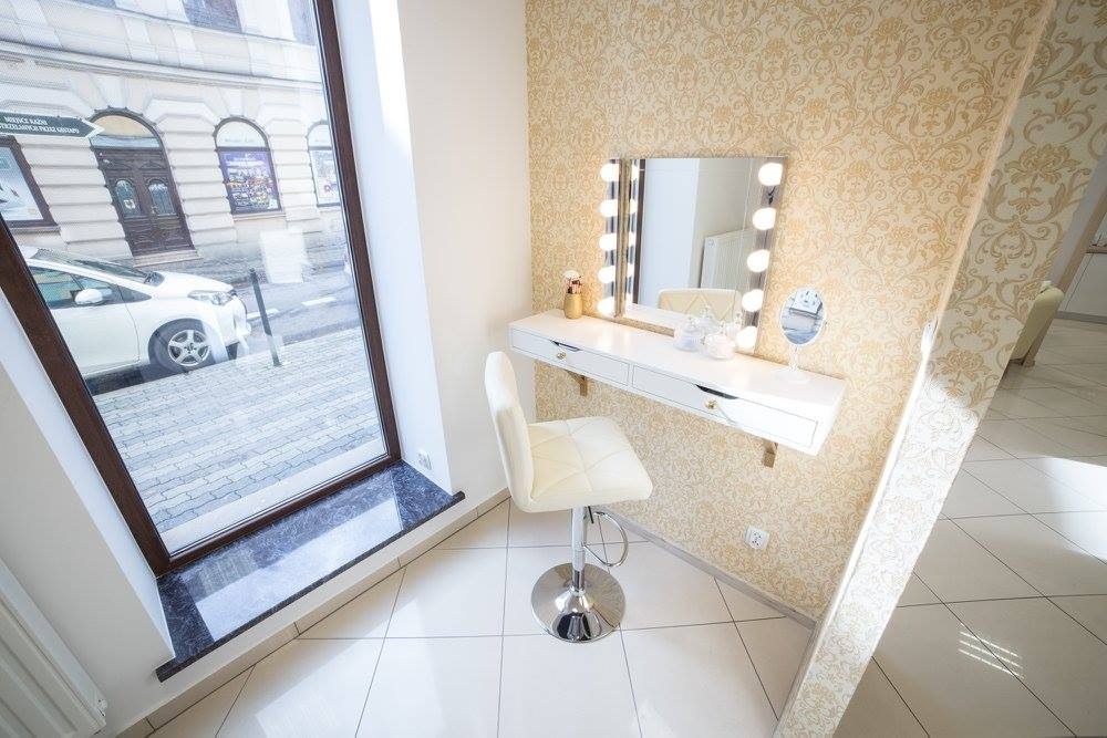 Jasne wnętrze: toaletka z oświetleniem, kremowe krzesło obrotowe, okno z widokiem na ulicę i zaparkowany samochód.