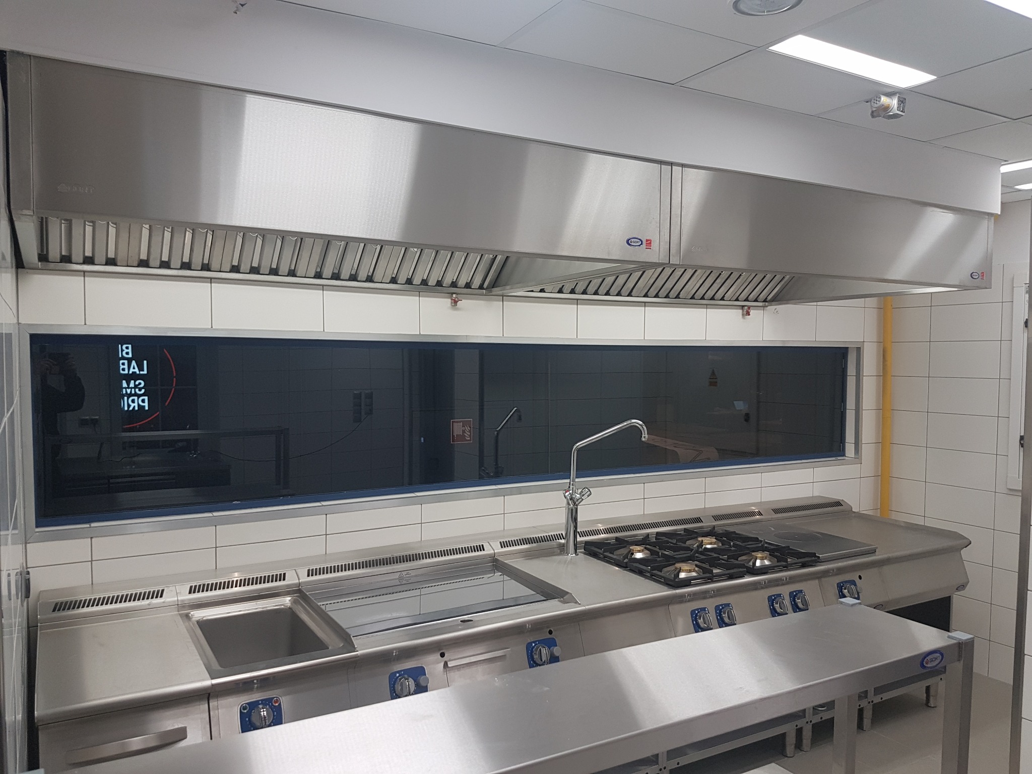 Profesjonalna kuchnia ze stali nierdzewnej z okapem, zlewozmywakiem, płytą grzewczą i stołem roboczym.