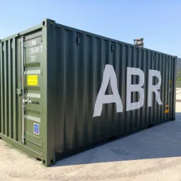 Nowy, oliwkowozielony kontener transportowy z białym napisem ABR, stojący na betonowym placu, w tle góra i inne kontenery.