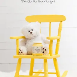 Żółte krzesełko bujane dla dziecka, pomalowane farbą Fusion Mineral Paint, z białym pluszowym misiem i puszką farby Tones for Tots w kolorze Little Star na siedzisku, na tle białej drewnianej ściany.