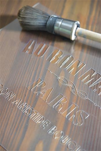 Szczotka do malowania leżąca na drewnianej desce z wygrawerowanym napisem 'AU BON MARCHE PARIS SON ARISTIDE BOUCICAUT'