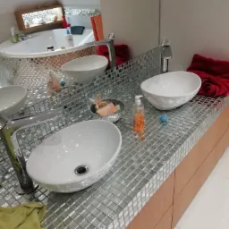 Umywalki nablatowe w nowoczesnej łazience wykończonej mozaiką lustrzaną, widoczna armatura, akcesoria i fragment wanny z obudową z mozaiki.