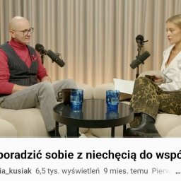 SEKSUOLOG TERAPEUTA PSYCHOLOG - Dwie osoby, mężczyzna w czerwonym golfie i kamizelce, kobieta w białej koszuli i spodniach w panterkę, siedzą na beżowej sofie. Przed nimi mikrofony i stolik z niebieskimi szklankami.