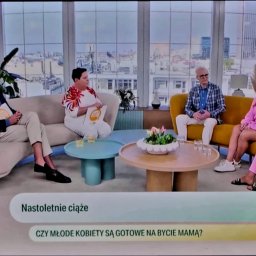 SEKSUOLOG TERAPEUTA PSYCHOLOG - Pięć osób (trzech mężczyzn i dwie kobiety) siedzi na beżowej i żółtej sofie w jasnym studiu telewizyjnym z widokiem na miasto, dyskutując o nastoletnich ciążach.