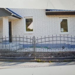 BAK-STAL - Czarne, metalowe ogrodzenie z dekoracyjnymi elementami przed domem z białej cegły.