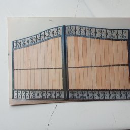 BAK-STAL - Zdjęcie drewnianej dwuskrzydłowej bramy z metalowymi zdobieniami, sfotografowanej na tle białej powierzchni.