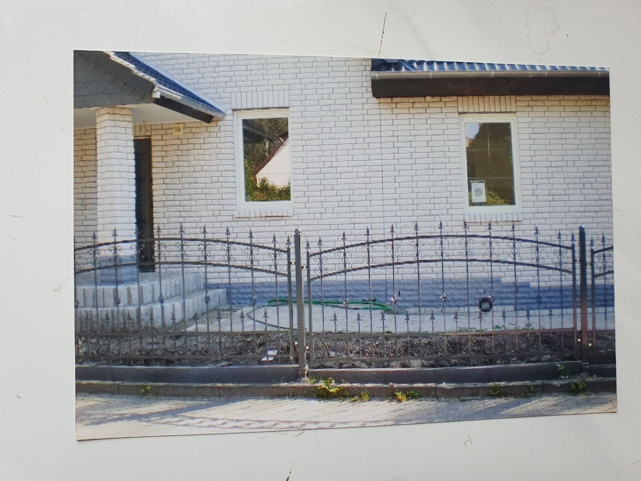 Czarne, metalowe ogrodzenie z dekoracyjnymi elementami przed domem z białej cegły.