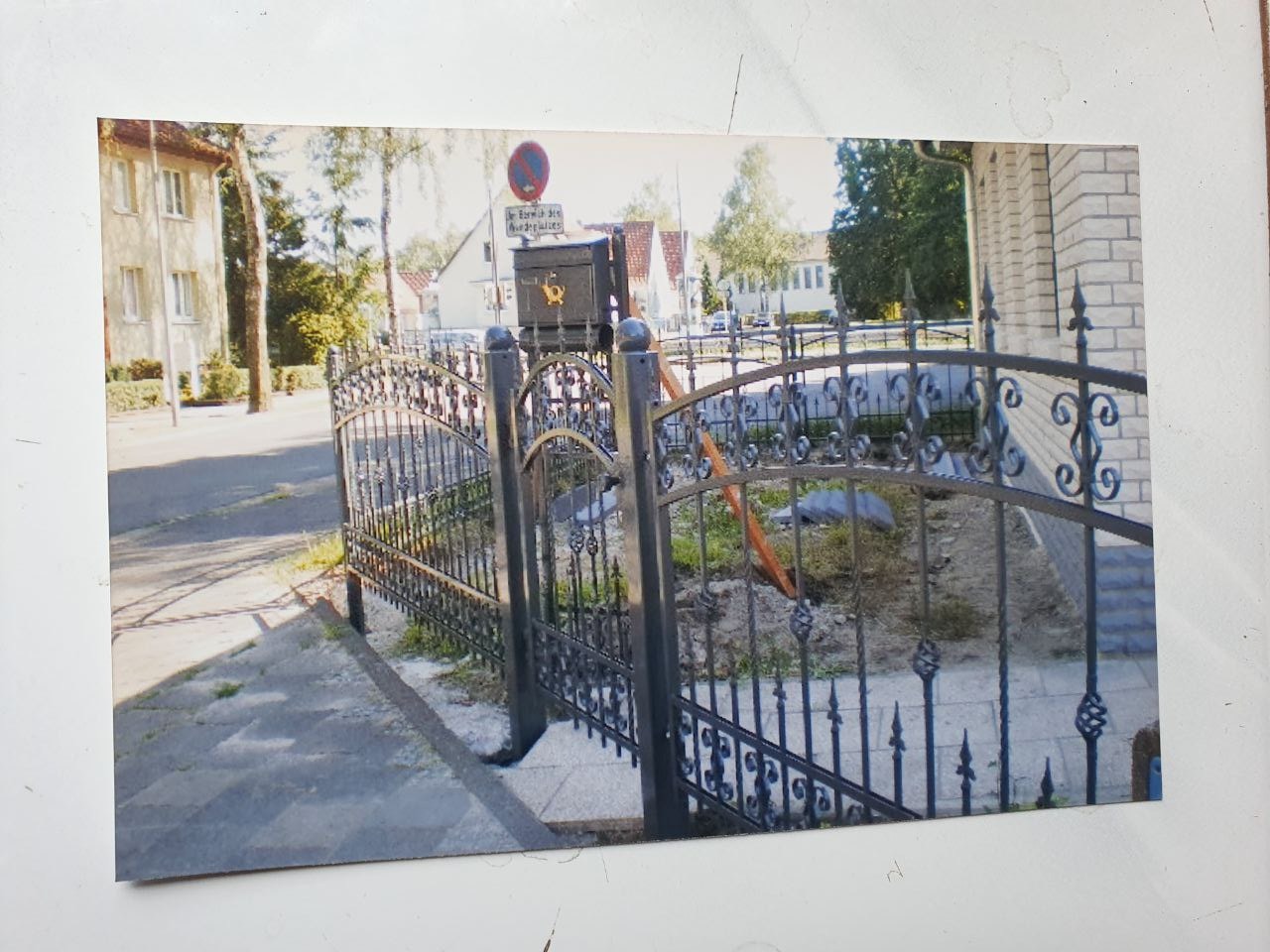 Kute, czarne ogrodzenie z dekoracyjnymi elementami, widoczne z zewnątrz posesji, z ulicą i budynkami w tle, w trakcie montażu.