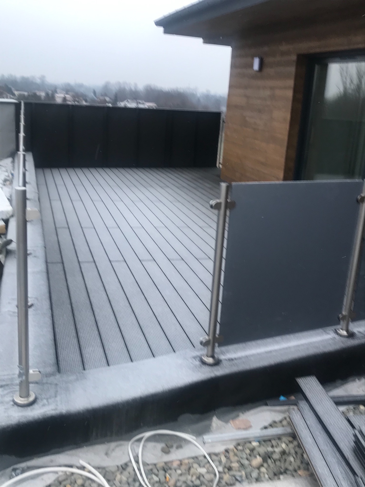 Nowoczesny taras z deski kompozytowej w Bielsku-Białej, z metalowymi balustradami i szarymi panelami, widok na zewnątrz w pochmurny dzień.