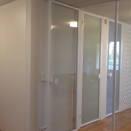 I.O.EXPERT Sp.zo.o - Białe, minimalistyczne wnętrze z przesuwnymi drzwiami z mlecznego szkła, drewnianą podłogą i dekoracyjnym panelem ściennym z wypukłymi elementami.