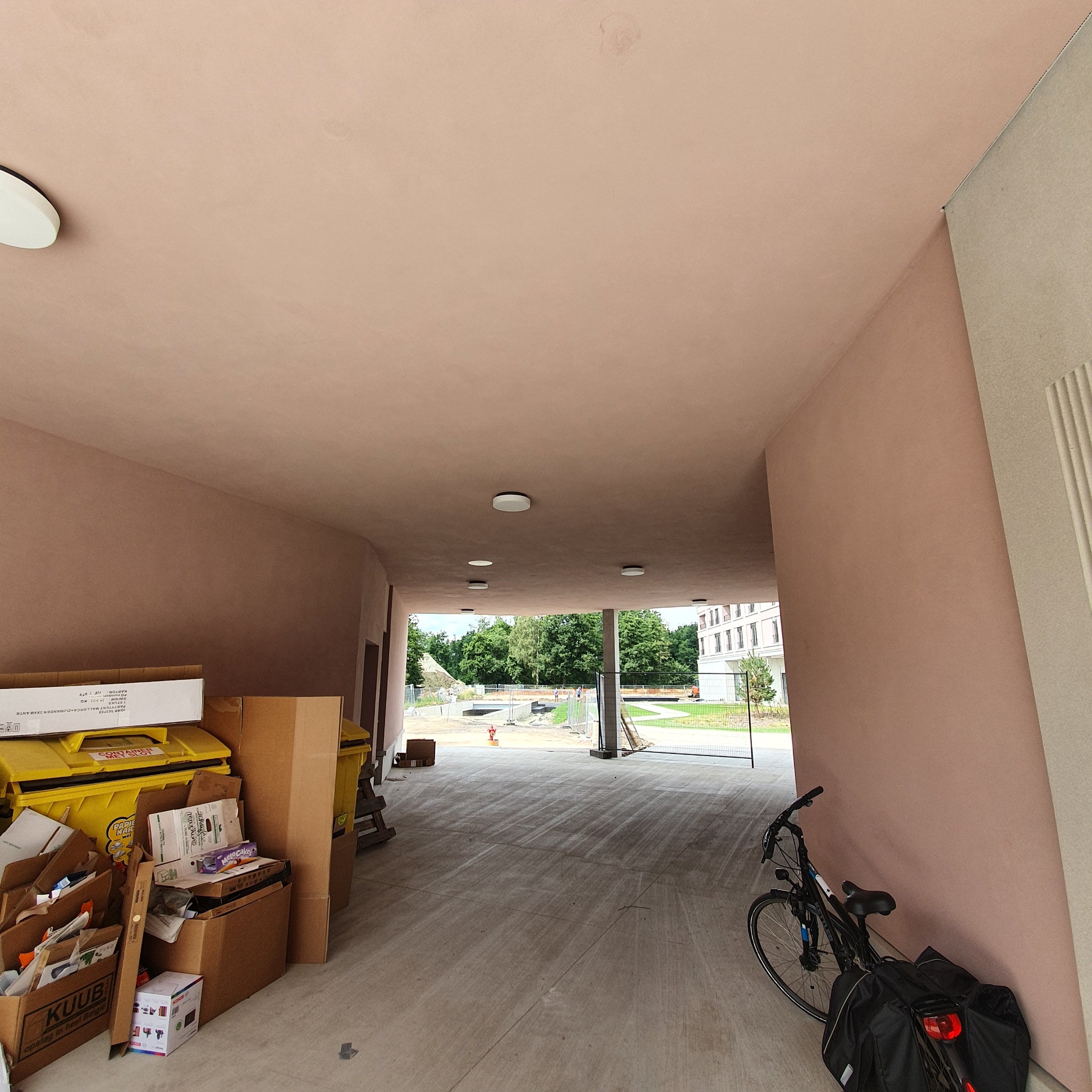 Nowo otynkowane przejście w budynku z widocznymi śladami prac budowlanych, workami i rowerem opartym o ścianę.