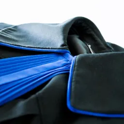 Toga prawnicza w kolorze czarnym z niebieską żabotem i wykończeniem, leżąca na białym tle.