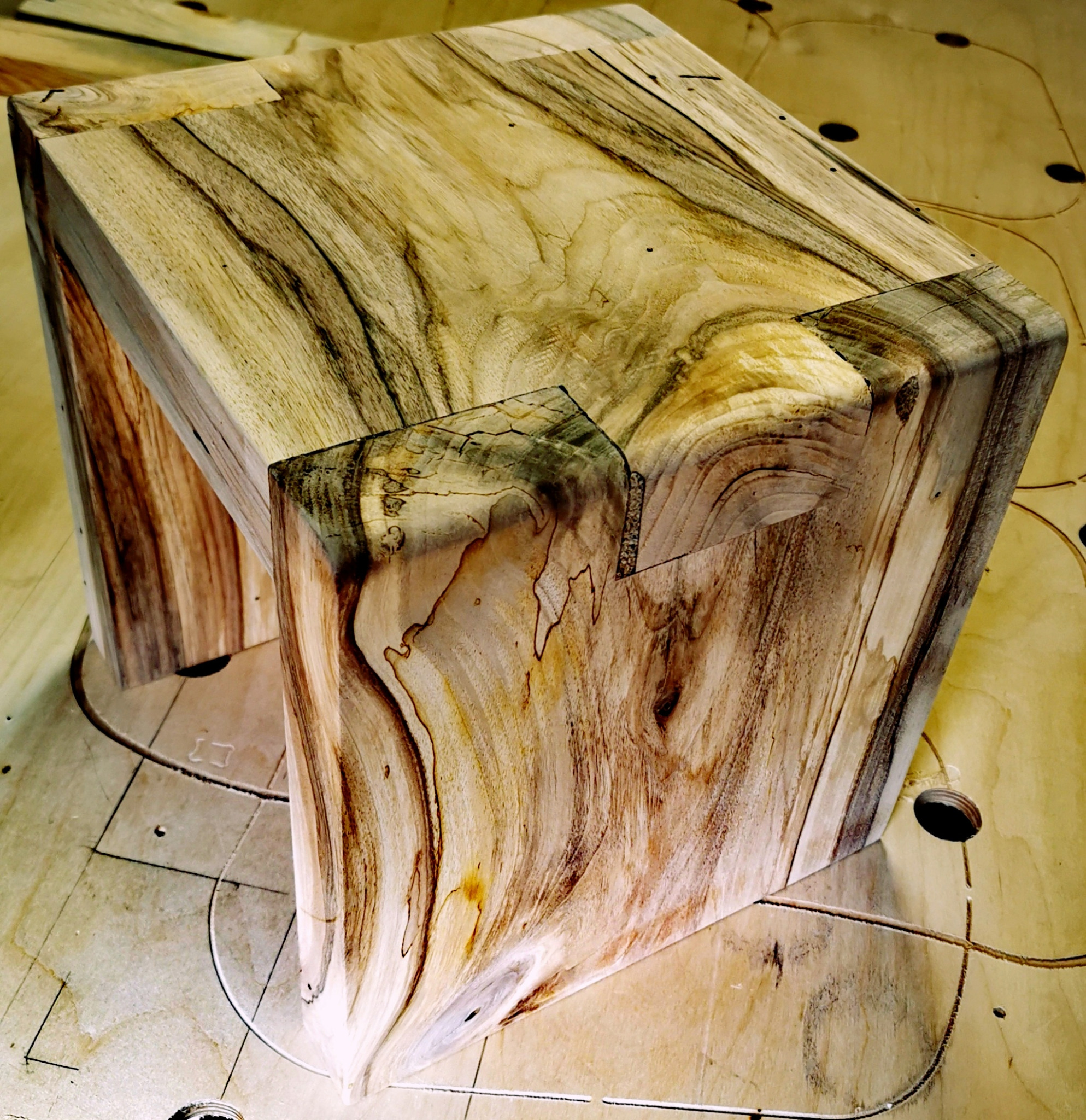 Drewniany taboret z widocznymi połączeniami stolarskimi, ukazujący unikalny rysunek słojów drewna na tle warsztatowego stołu.