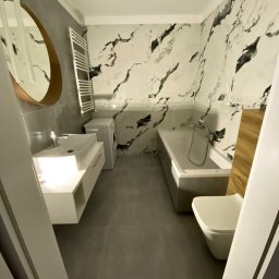 Usługi remontowo budowlane Jędrocha - Nowoczesna łazienka po remoncie z marmurowymi płytkami na ścianach, umywalką z szafką, grzejnikiem drabinkowym, wanną i toaletą.