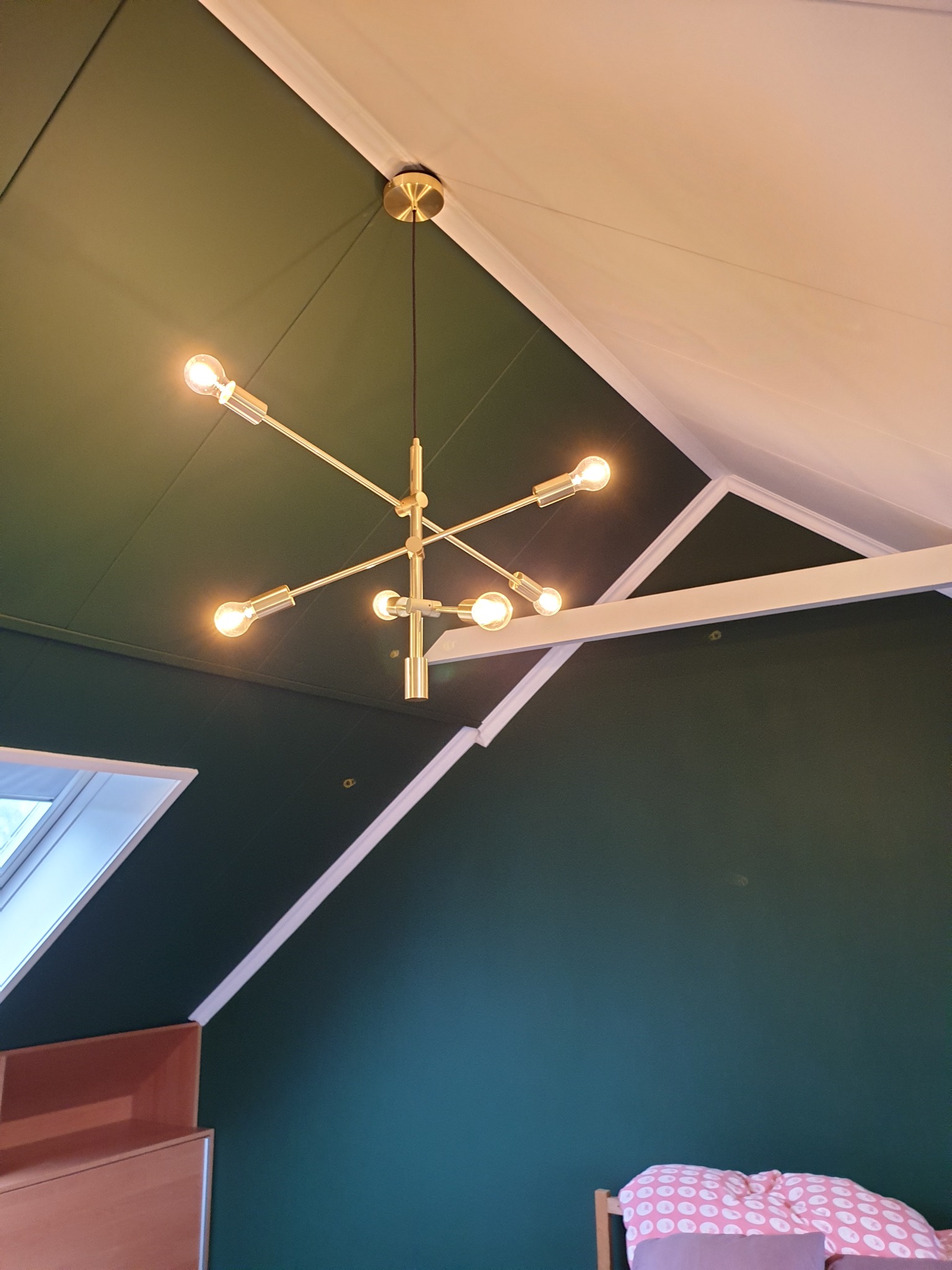 Nowoczesna, złota lampa sufitowa z odsłoniętymi żarówkami w pokoju z ciemnozielonymi ścianami i skośnym sufitem.
