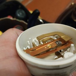 Serwis AGD w Szczecine - Detale wewnętrzne elementu grzejnego, prawdopodobnie z piekarnika, widoczne w białej obudowie trzymanej w dłoni, z miedzianymi i stalowymi elementami oraz sprężyną.