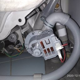 Serwis AGD w Szczecine - Wnętrze zmywarki z widoczną pompą obiegową, wężem odpływowym i elementami elektrycznymi, ukazujące proces naprawy lub wymiany części.