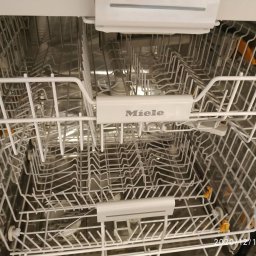 Serwis AGD w Szczecine - Wnętrze zmywarki Miele z wysuwanymi koszami i charakterystycznymi pomarańczowymi elementami mocującymi naczynia.