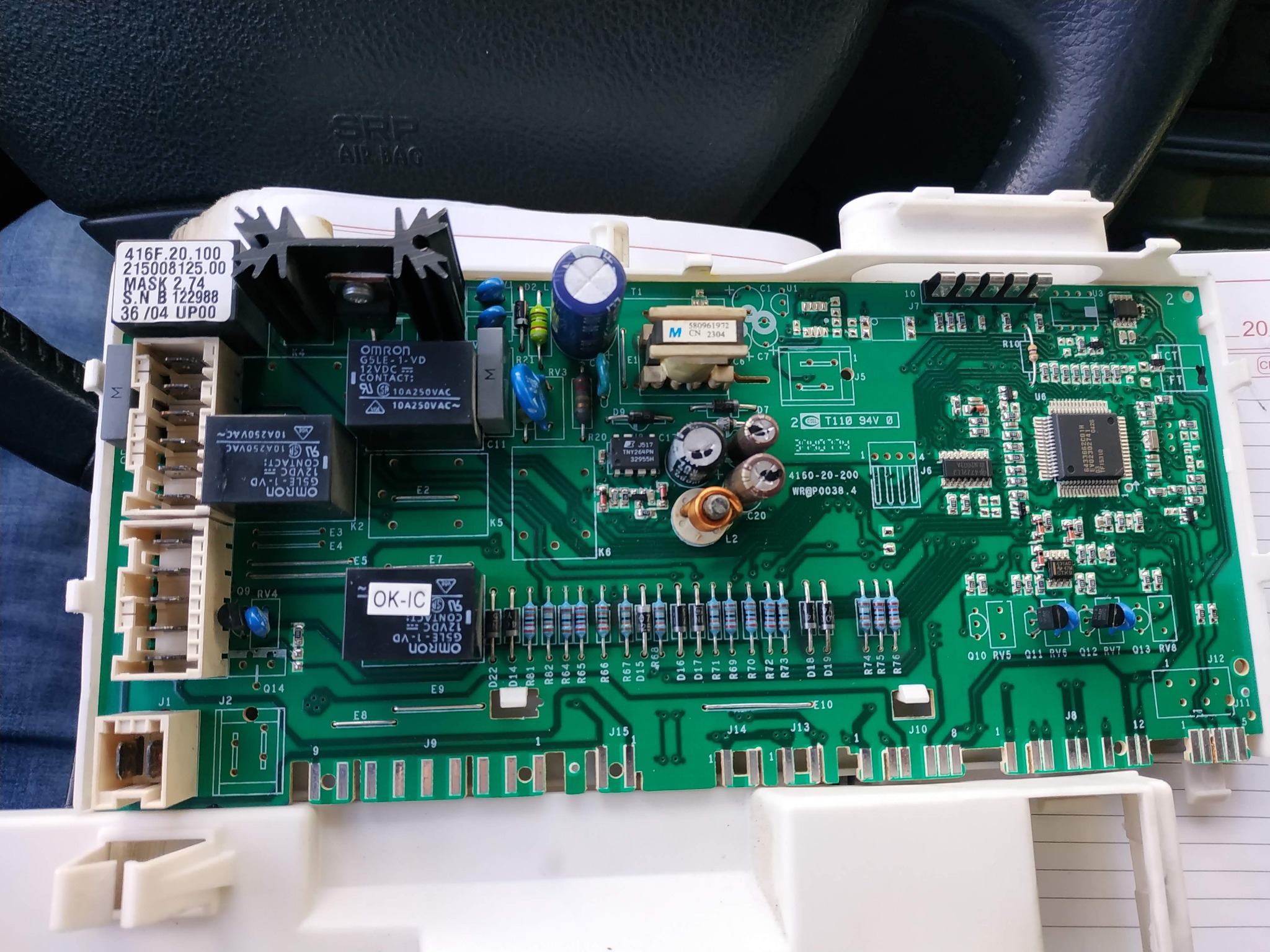 Zdjęcie zbliżeniowe zielonej płytki drukowanej z licznymi elementami elektronicznymi, takimi jak kondensatory, rezystory i układy scalone, umieszczonej na białej plastikowej ramce, z widocznymi...