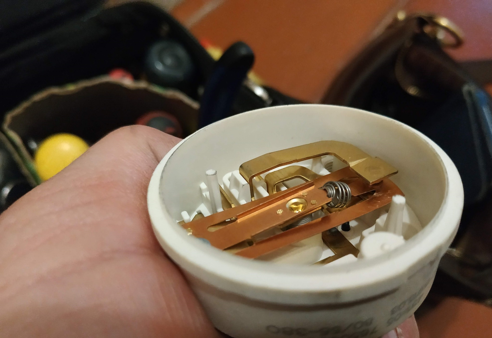 Detale wewnętrzne elementu grzejnego, prawdopodobnie z piekarnika, widoczne w białej obudowie trzymanej w dłoni, z miedzianymi i stalowymi elementami oraz sprężyną.