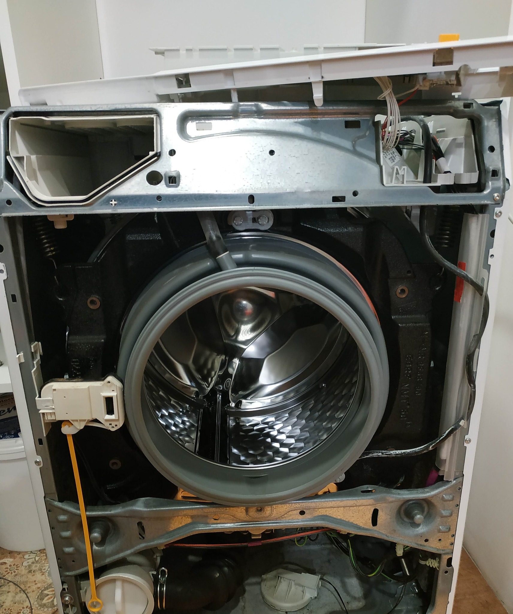 Wnętrze pralki z otwartą obudową, widoczny bęben, uszczelka i elementy mechaniczne, podczas przeglądu lub naprawy.