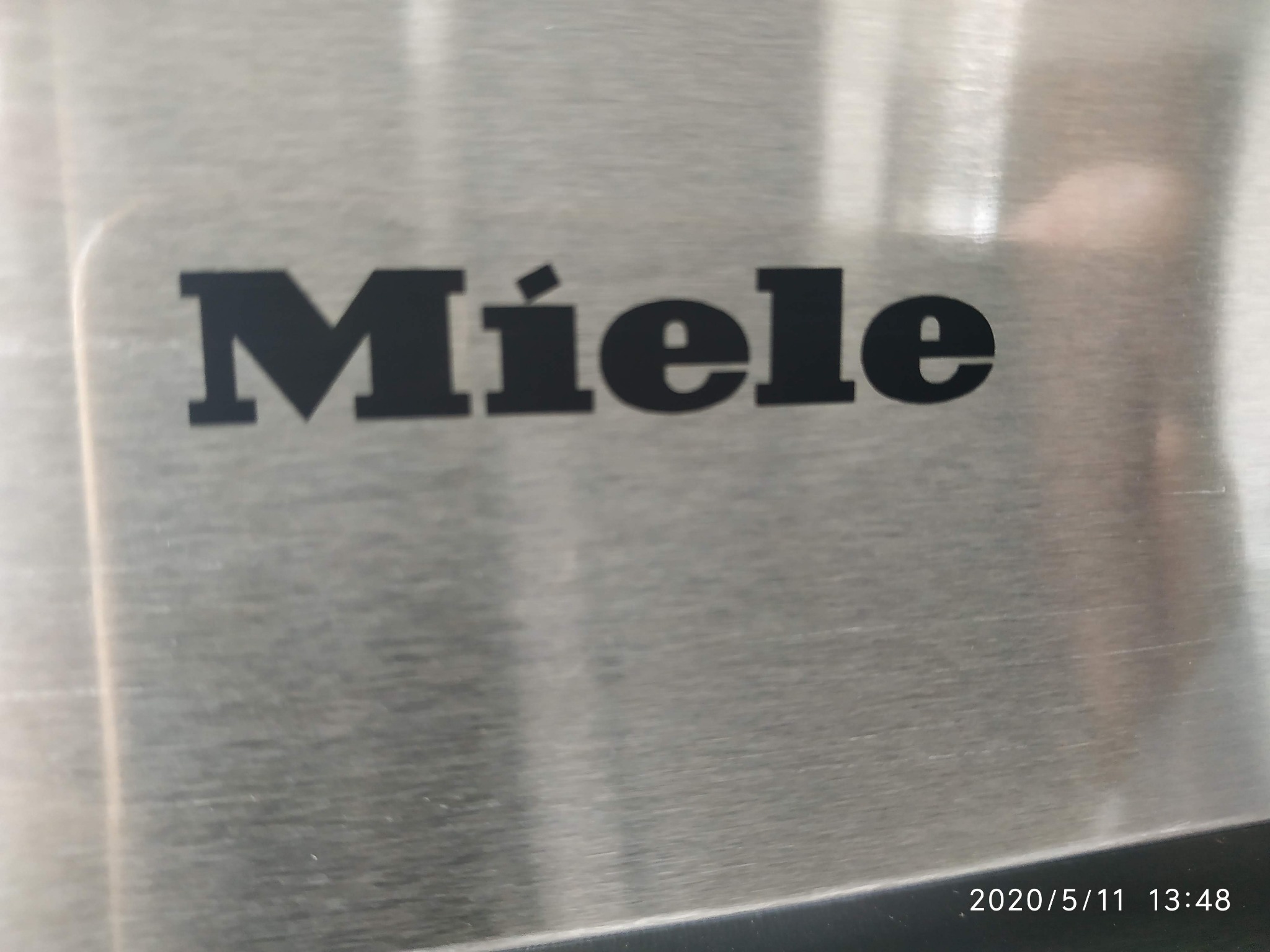 Logo Miele na szczotkowanej metalowej powierzchni urządzenia AGD, z widoczną datą i godziną wykonania zdjęcia w prawym dolnym rogu.