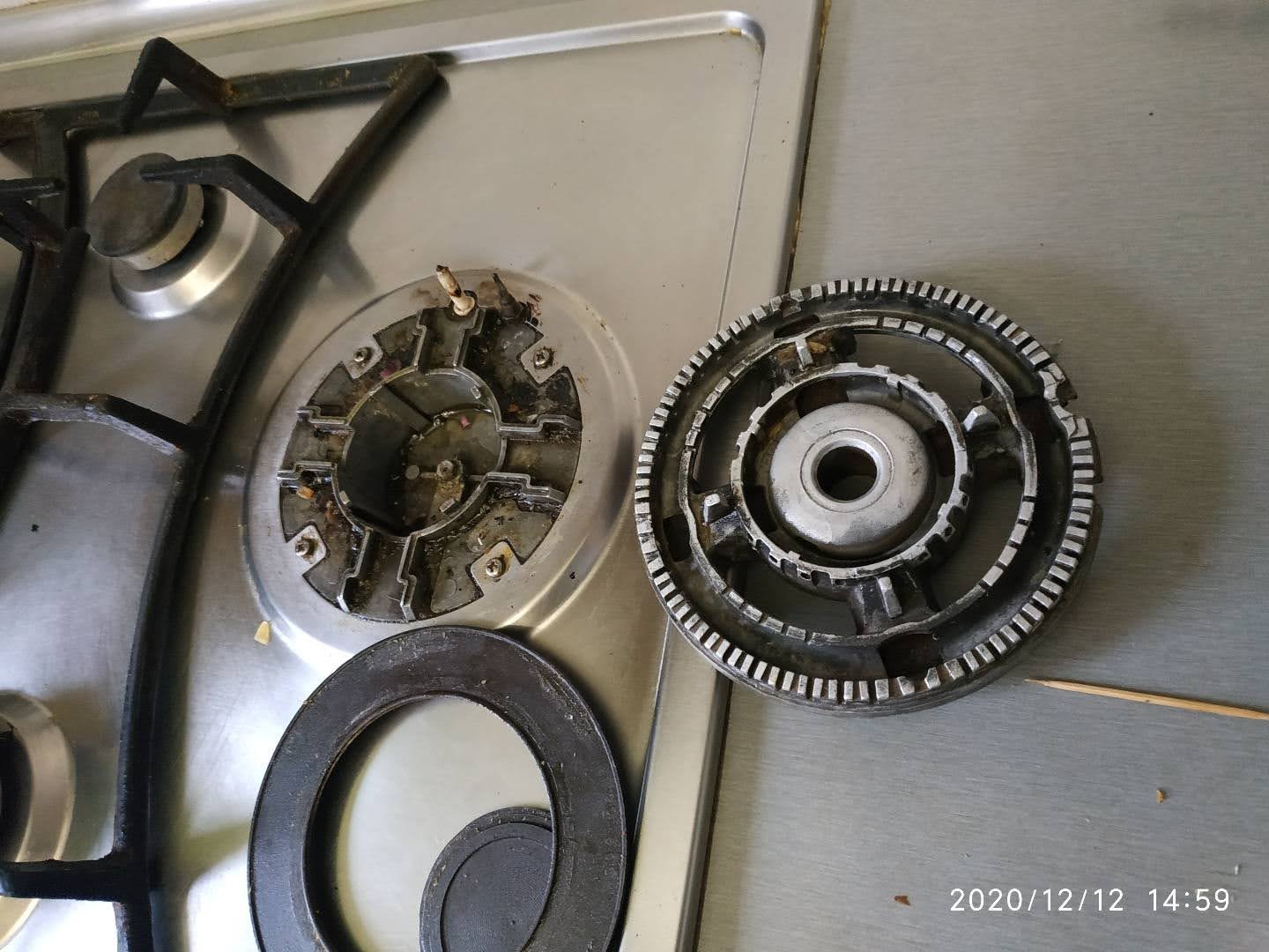 Rozłożona kuchenka gazowa: palnik z pozostałościami po gotowaniu, obok elementy rozłożone na blacie ze stali nierdzewnej. Widoczny fragment rusztu.