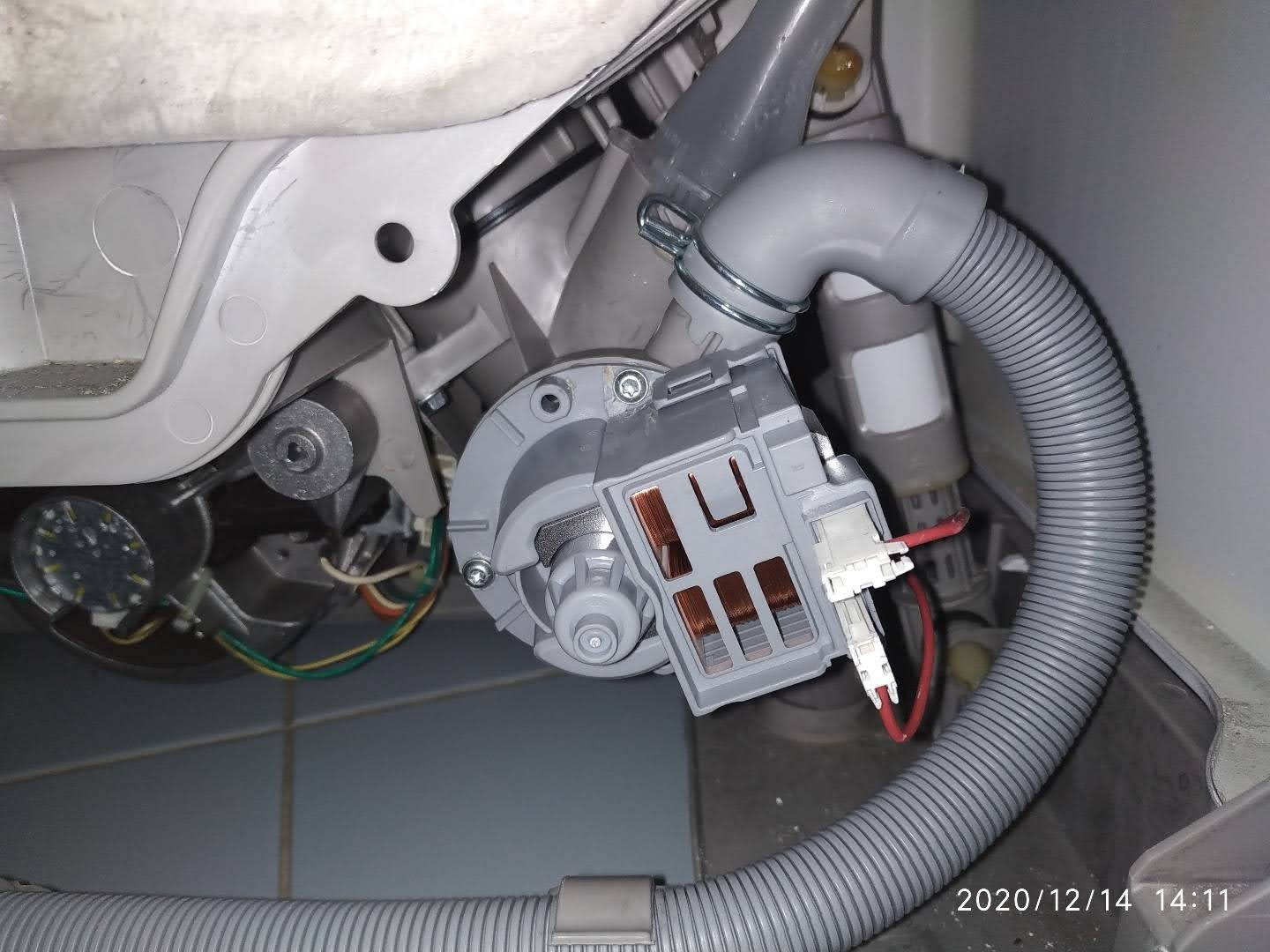 Wnętrze zmywarki z widoczną pompą obiegową, wężem odpływowym i elementami elektrycznymi, ukazujące proces naprawy lub wymiany części.