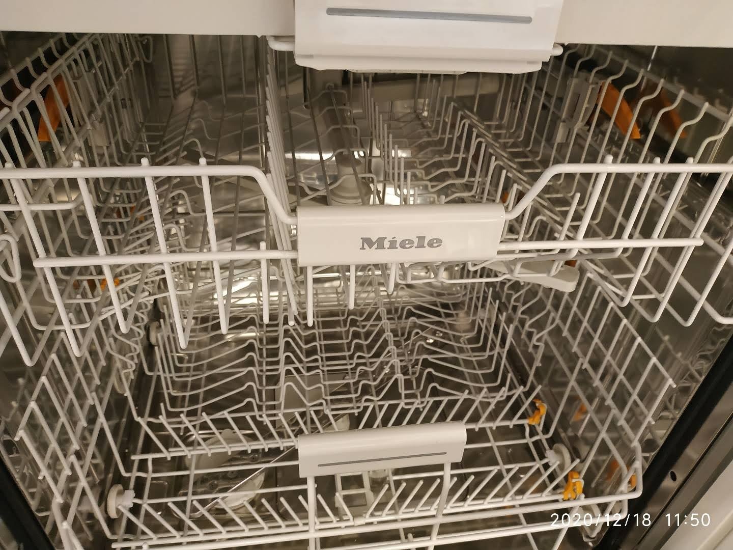 Wnętrze zmywarki Miele z wysuwanymi koszami i charakterystycznymi pomarańczowymi elementami mocującymi naczynia.