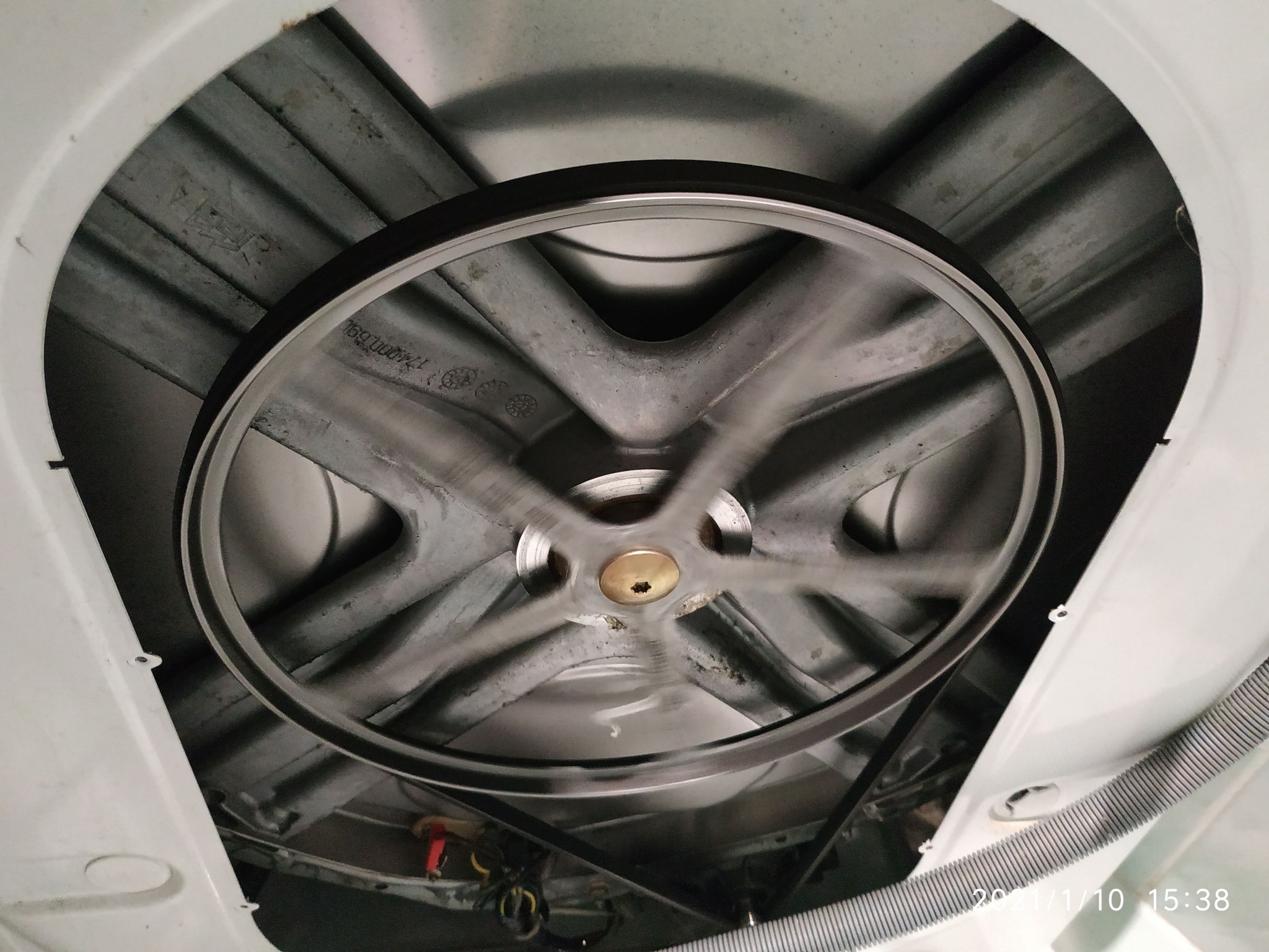 Wnętrze pralki z widocznym bębnem, paskiem napędowym i elementami konstrukcyjnymi, ukazujące mechanizm w trakcie pracy z efektem rozmycia ruchu.