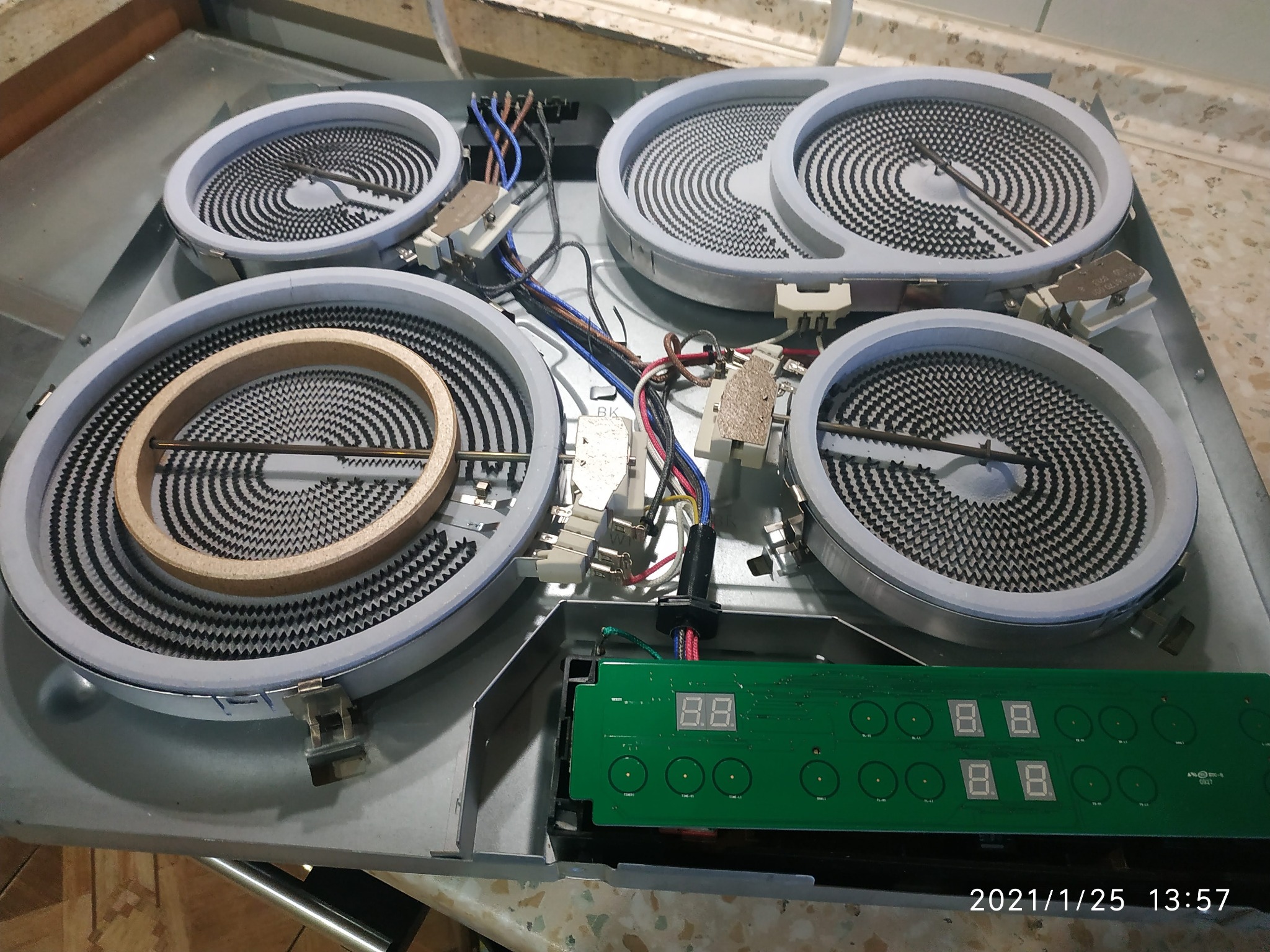 Otwarta płyta indukcyjna z widocznymi elementami grzejnymi, okablowaniem i płytką sterującą z wyświetlaczem cyfrowym, w trakcie naprawy.