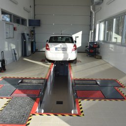 WULKAN S.C. M. Pasoń, G. Jabłoński - Biały samochód osobowy na stanowisku diagnostycznym w jasnym warsztacie. Widoczny kanał rewizyjny z podnośnikami i osprzęt diagnostyczny.