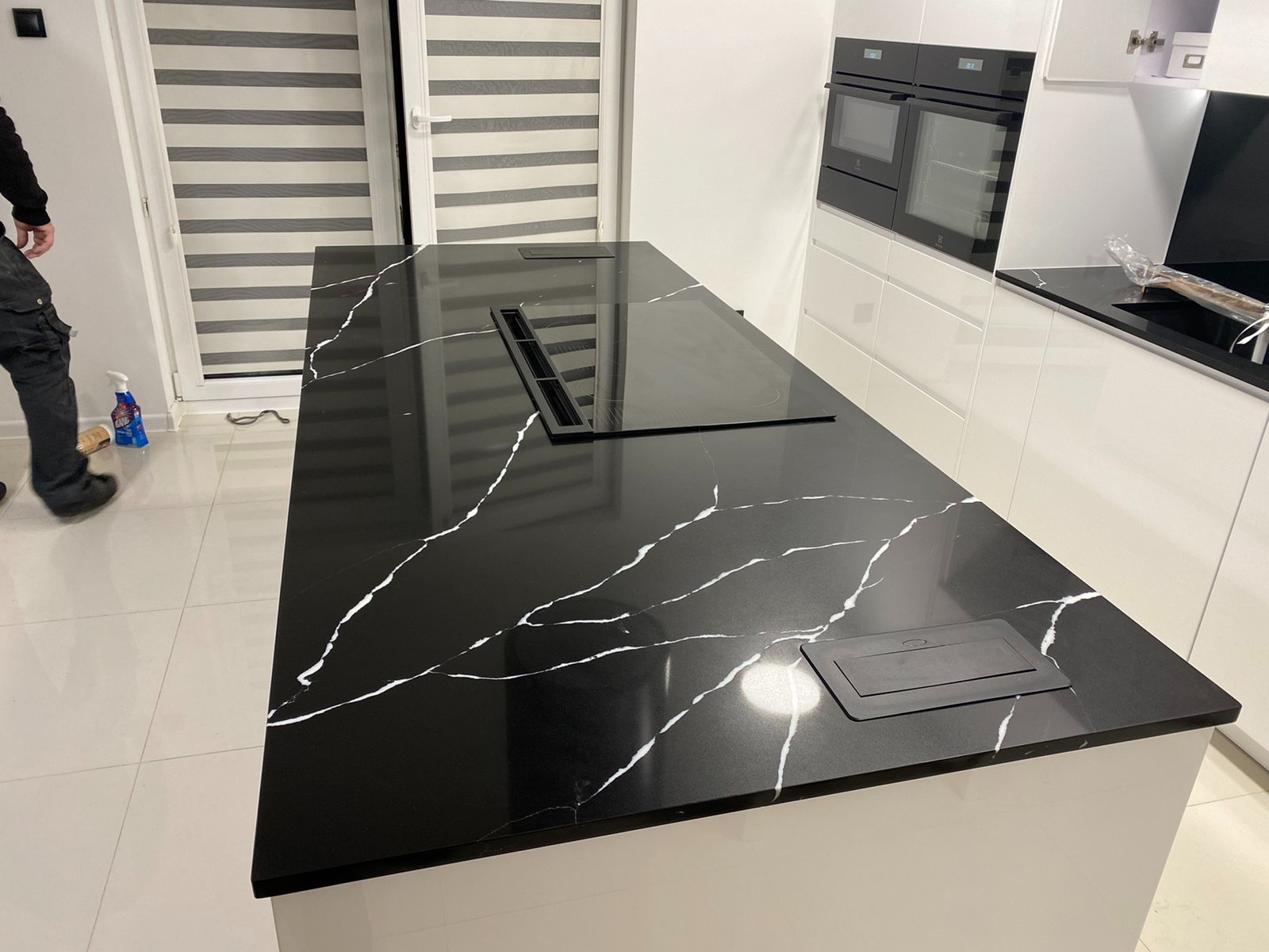 Czarny blat z białym żyłkowaniem, wbudowana płyta indukcyjna i gniazdo elektryczne, nowoczesna kuchnia z białymi szafkami.