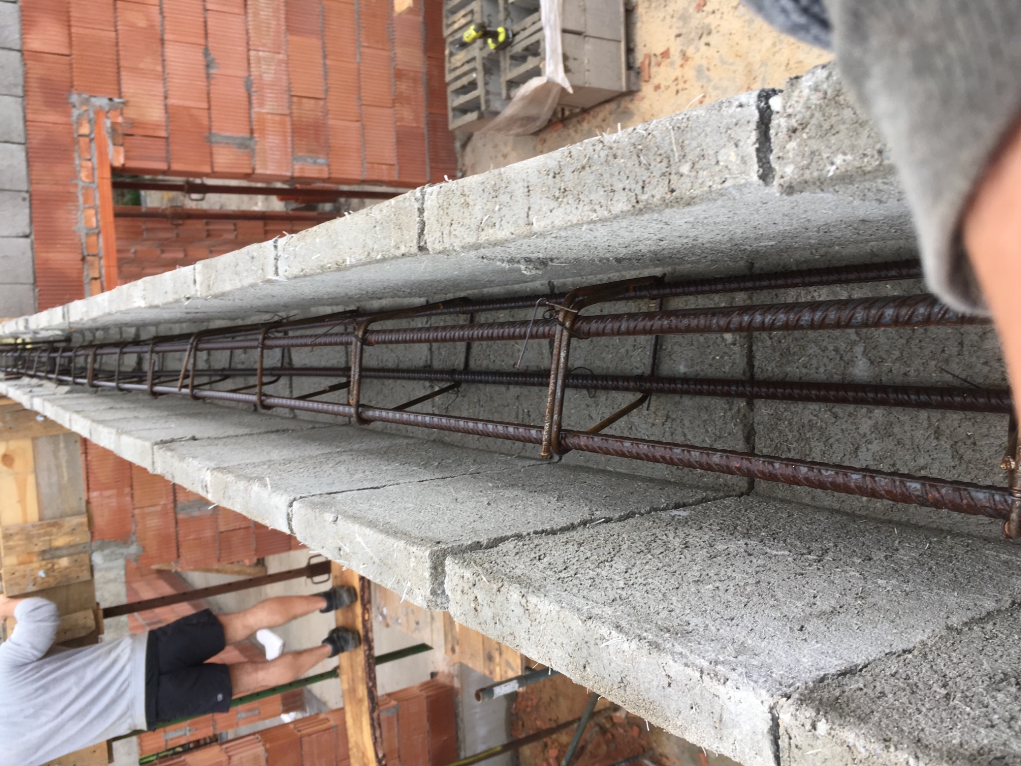 Wieniec żelbetowy w trakcie wykonywania, z widocznym zbrojeniem i betonowymi bloczkami, w tle ceglana ściana.