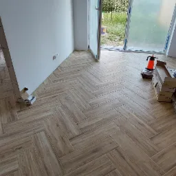 Układanie paneli podłogowych w jodełkę w Brzegu Dolnym, widoczne puszki z farbą, kartony z panelami i narzędzia pracy.