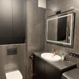 Nowoczesna łazienka w odcieniach szarości z podświetlanym lustrem, umywalką nablatową z miedzianą baterią i pralką Electrolux.