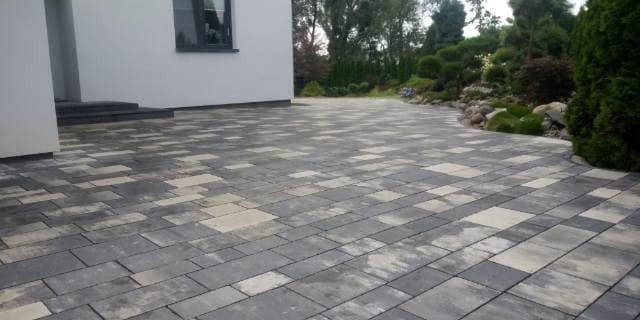 Ułożona kostka brukowa w Naruszewie przed budynkiem z wejściem po schodach, widoczny fragment ogrodu z roślinnością.