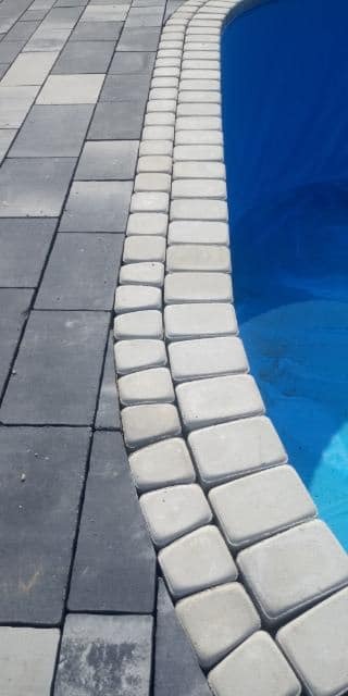 Szara kostka brukowa ułożona obok basenu, z jasnymi obrzeżami z kostki.