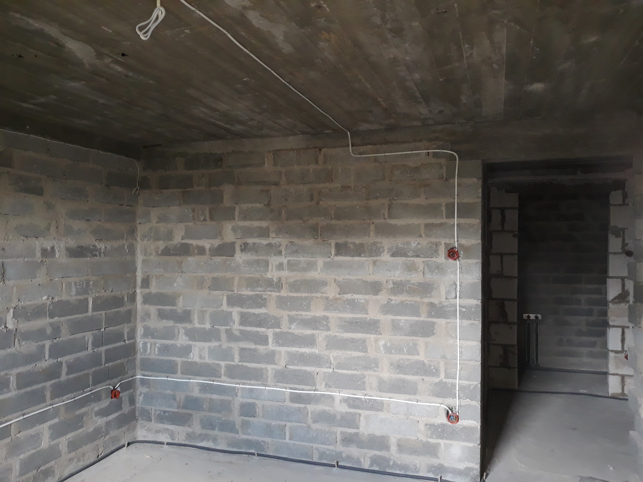 Surowy mur z bloczków betonowych z widocznymi przewodami elektrycznymi i puszkami instalacyjnymi w trakcie montażu, widok wnętrza w stanie deweloperskim.