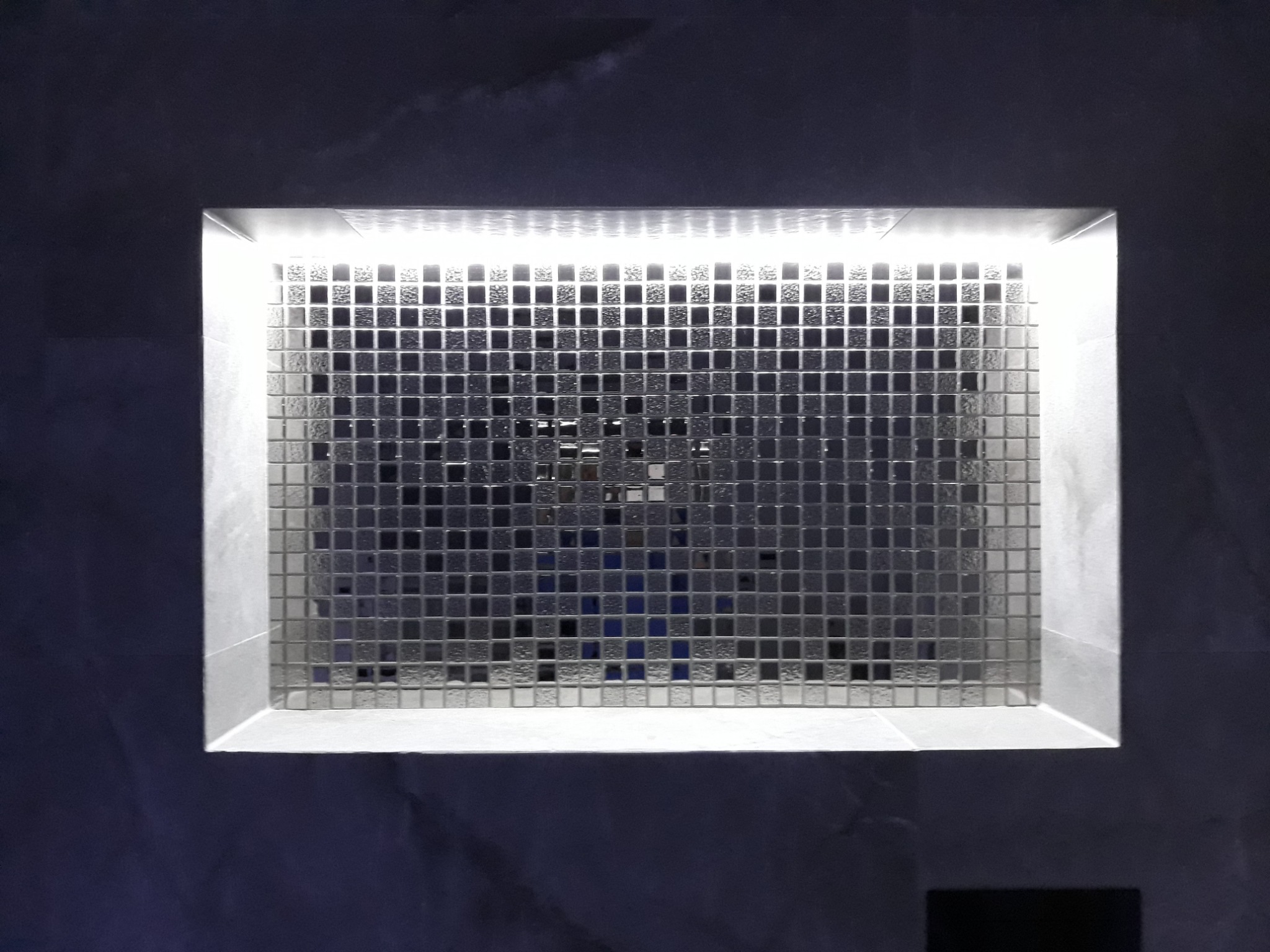 Wnęka oświetleniowa z mozaiką w ciemnej łazience, podświetlona listwą LED na górze.