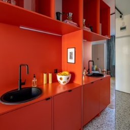 Fresh Home - Nowoczesna kuchnia w intensywnym odcieniu czerwieni z czarnym zlewem i armaturą, uzupełniona otwartymi półkami i owocami w dekoracyjnej misie.